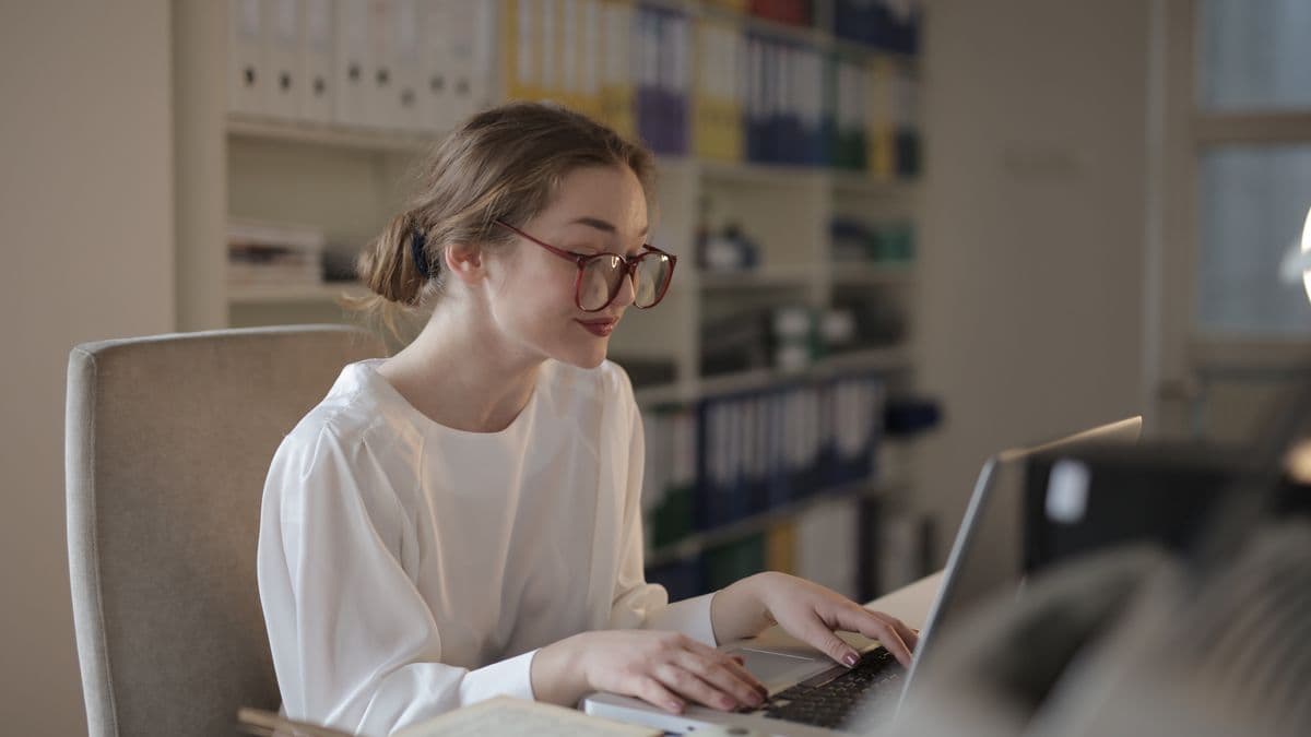A woman working at a laptop beside shelves of files and folders
