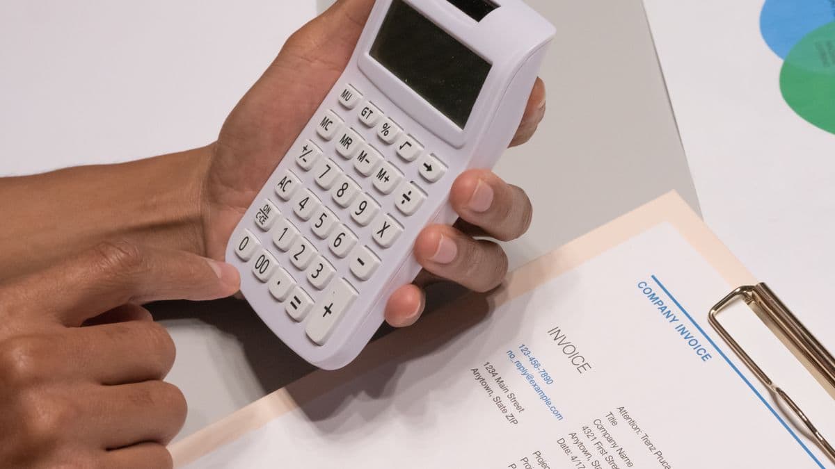 A hand using a calculator on top of a company invoice