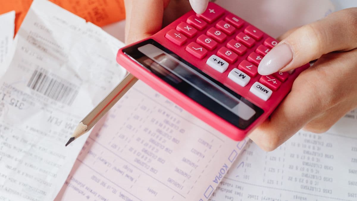A hand using a calculator over printed invoices and receipts